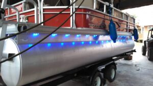 boat2 A red and silver pontoon boat with blue LED lights along the side, sitting on a trailer indoors.