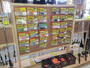 bt 10 Display board with various fishing lures in yellow packs, fishing rods on the sides, and bins of red bobbers below.