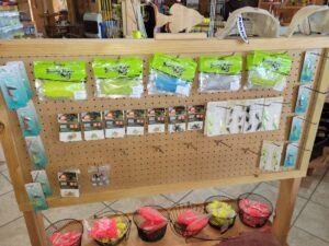 bt 11 Fishing lures and bait packs displayed on a wooden pegboard, with baskets of fishing floats on the shelf below.