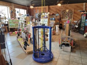 bt 3 Fishing rods on a blue stand in a shop with various fishing gear and supplies on shelves and displays.