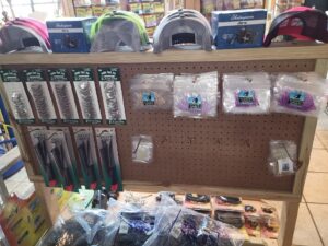 bt 6 Fishing tackle display with hooks, lures, pliers, hats, and various fishing accessories on a wooden pegboard.