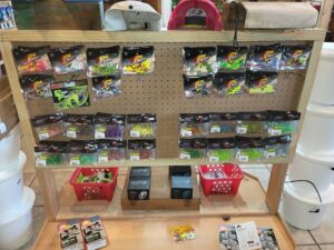 bt 8 Fishing lures and tackle supplies displayed on a wooden pegboard stand with baskets and boxes below.