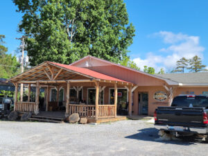 bt1 A one-story building with a wooden porch, parked truck, and visible "OPEN" sign on a sunny day.