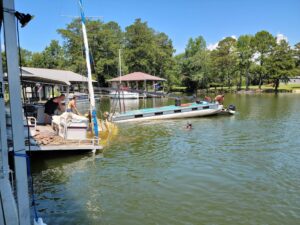 towing 5 People are relaxing on a dock and boat near the shore; one person is swimming in the lake on a sunny day.